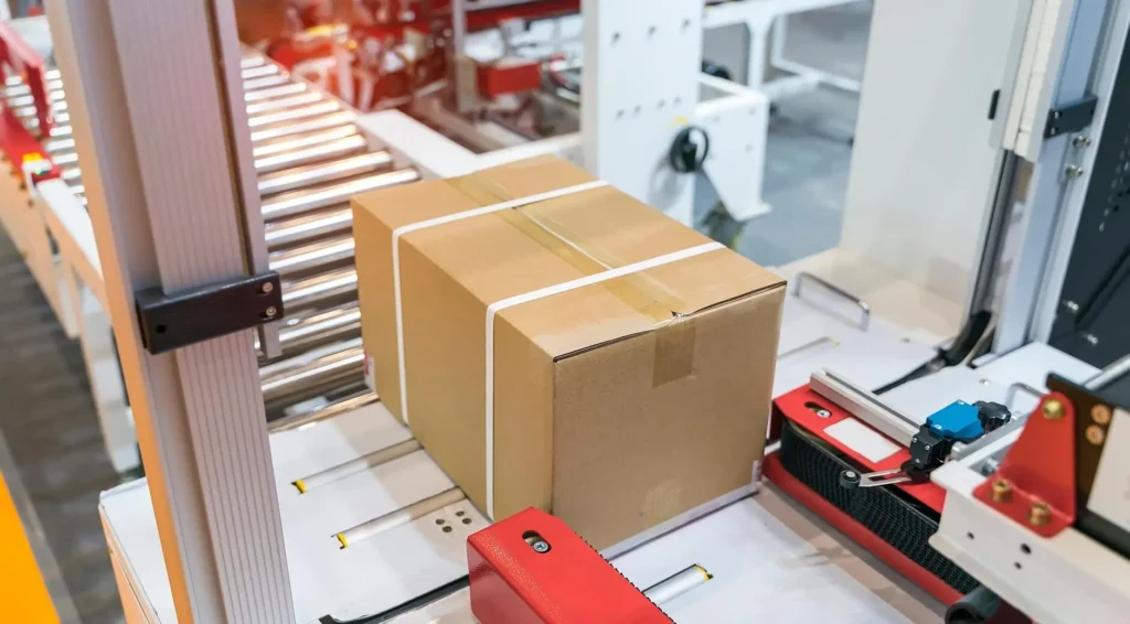 Sealed cardboard boxes moving along a roller conveyor belt in an automated warehouse or distribution facility.